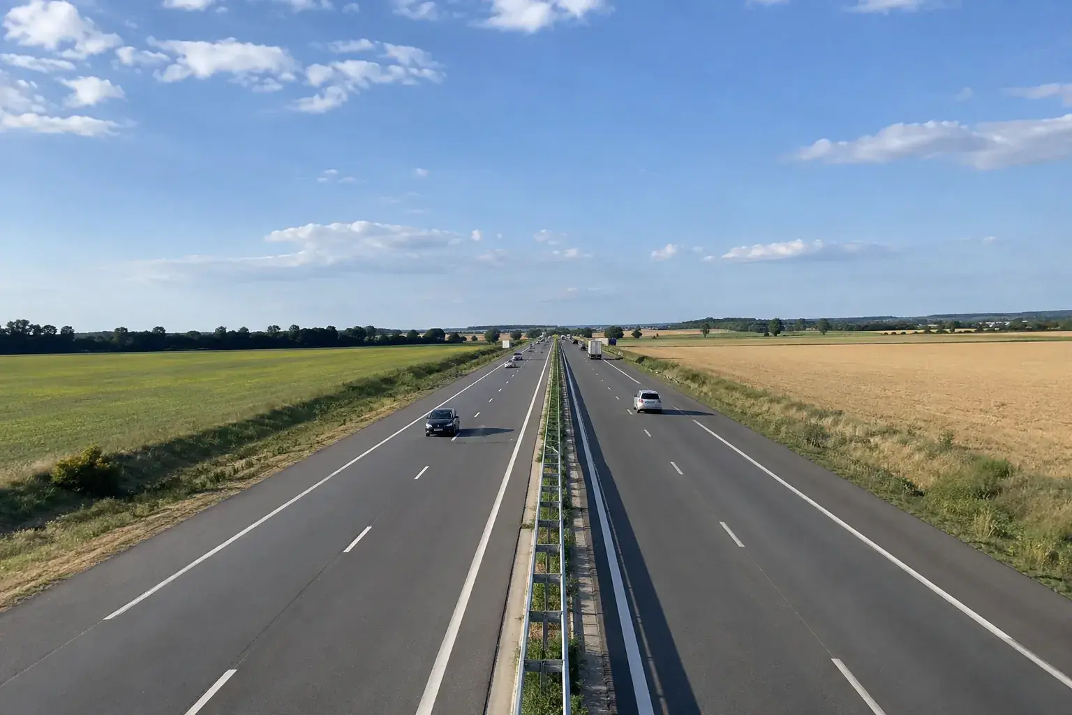Une autoroute à deux fois deux voies traversant de grandes plaines agricoles, vue d’un pont, sous un ciel bleu