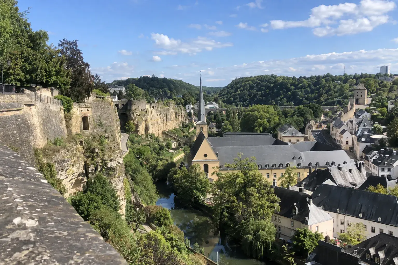 La vieille ville de Luxembourg vue de la Corniche : remparts de pierre, toits d’ardoise du Grund et vallée verte de l’Alzette sous un ciel bleu