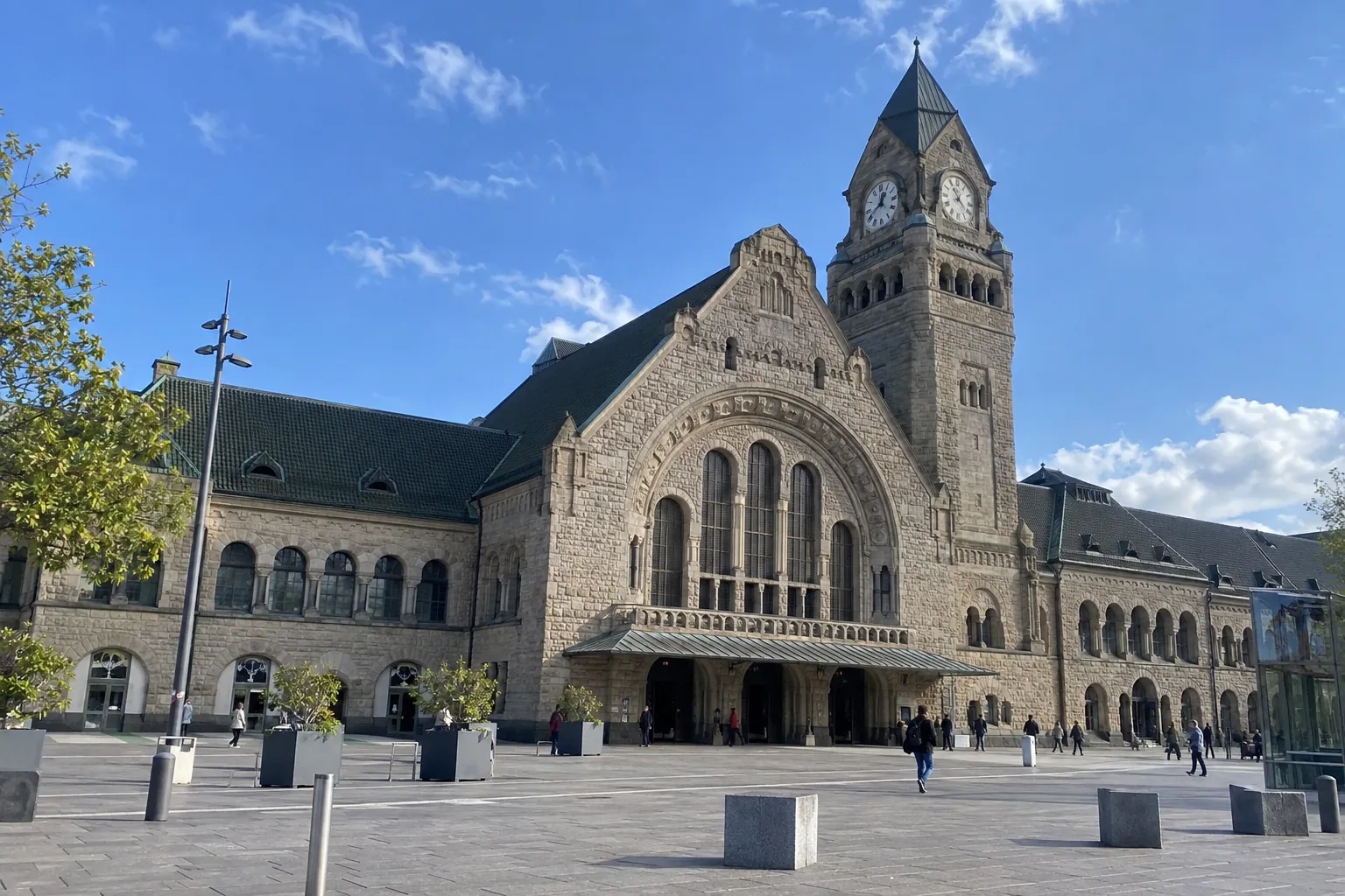 La façade de la gare de Metz-Ville, en pierre claire, avec sa tour d’horloge, sous un ciel bleu